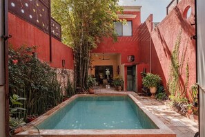 A courtyard with a pool, surrounded by red walls and various plants. - Casa Ambos Mundos en Merida Yucatan (Mérida)