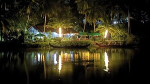 A riverside restaurant with a thatched-roof structure, boats, and palm trees. - Kadingis homestay and eco tourism (Kadalundi)