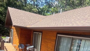 A wooden deck with outdoor furniture, a sliding glass door, and a view of trees. - Daggett Lake Cabin with Dock & Beach (Crosslake)