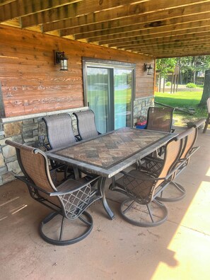 A covered patio with a stone wall, a glass sliding door, and a metal table with chairs. - Daggett Lake Cabin with Dock & Beach (Crosslake)