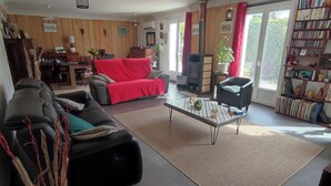 A living room with a sofa, a red chair, a coffee table, and a bookshelf. - House with swimming pool in the heart of the seaside resort of Ronce /La Tremblade (La Tremblade)