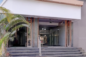Une entrée moderne, avec des marches menant à une porte en verre, un ventilateur de plafond et un espace intérieur visible, doté d’étagères.