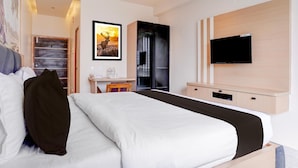 Une chambre d’hôtel avec un grand lit, un bureau avec une chaise, un téléviseur à écran plat fixé au mur et un tableau encadré au-dessus du bureau.