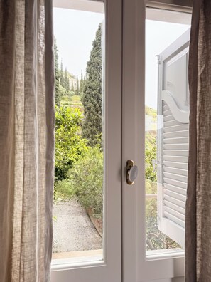 Eine Tür mit Blick auf einen Garten, eine weiße Außenwand und ein Fenster mit Jalousien.