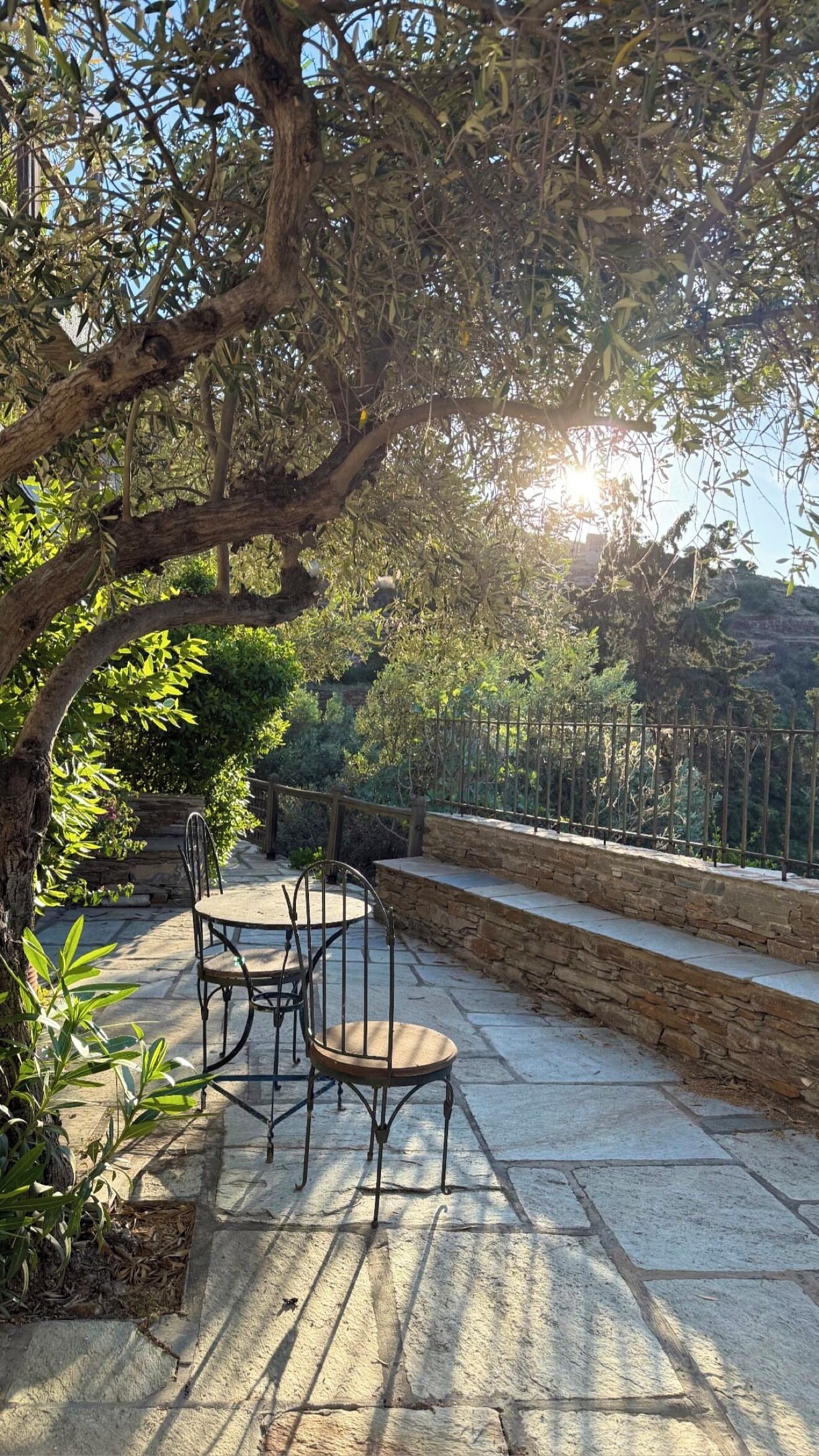 An outdoor patio with stone flooring, metal chairs, and a stone wall.