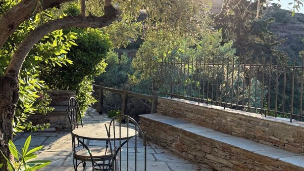 An outdoor patio with stone flooring, metal chairs, and a stone wall. - Large Villa with Pool and Private Tennis Court near Ormos Korthiou (Ormos Korthiou)