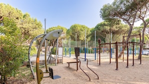 An outdoor exercise area with various fitness equipment, surrounded by trees and a fence. - Jesolo Family Resort (Jesolo)