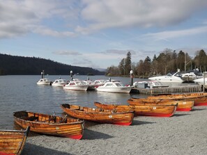 A marina with boats docked, a sandy shore, and a forested hill in the background. - Wilders Wood (Windermere)