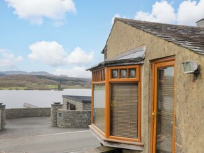 A building with a stone wall, a wooden door, and a window overlooking a lake. - Wilders Wood (Windermere)