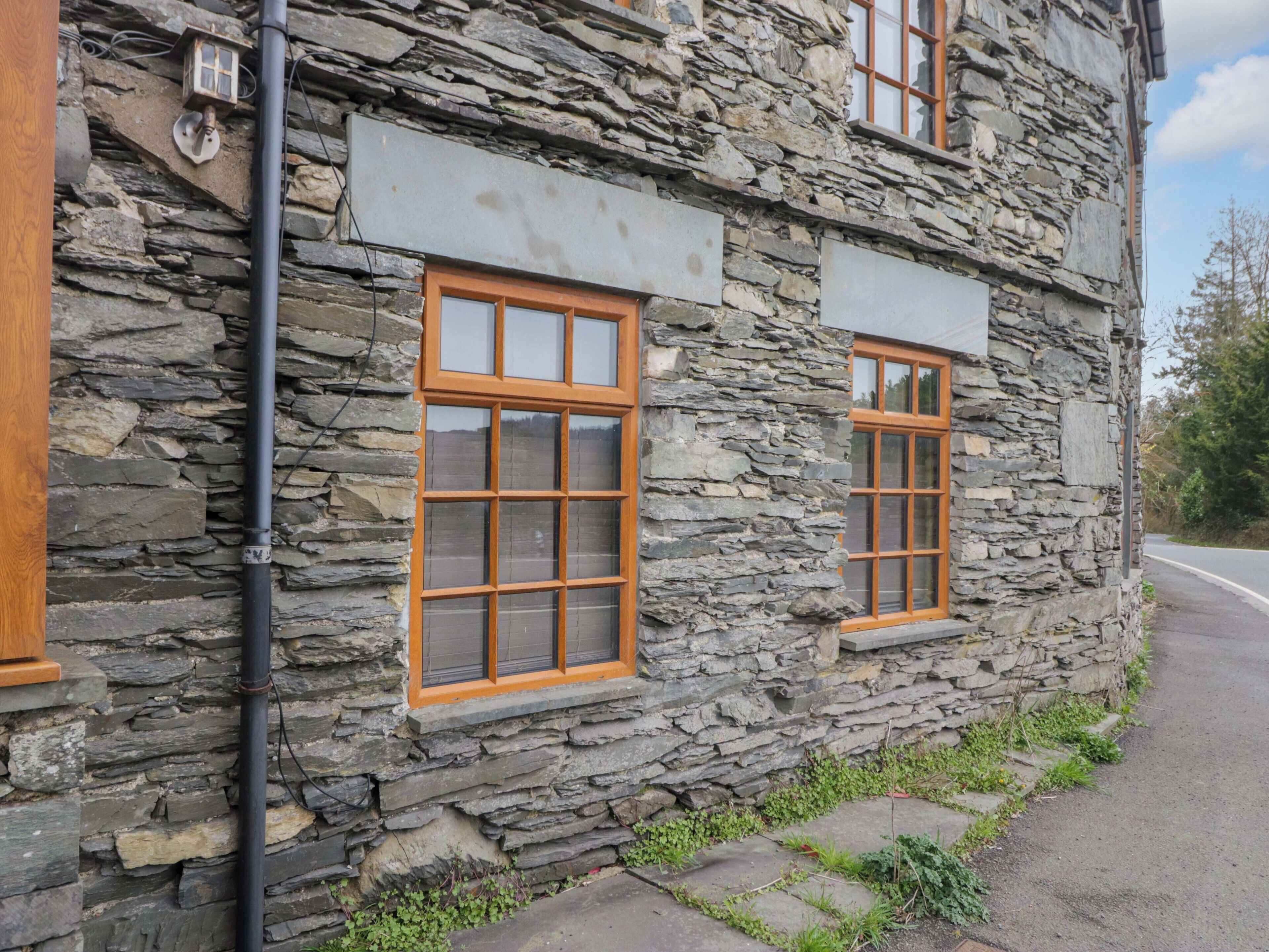 Ein Steinhaus mit zwei Fenstern, einem sichtbaren Stromkabel und einem gepflasterten Weg.