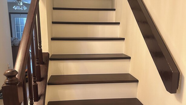 Una scala con gradini scuri e una ringhiera in legno, che conduce a un piano superiore.