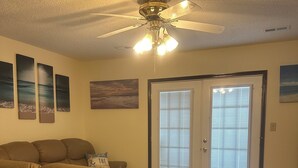 Un soggiorno con un ampio divano beige, una ventola a soffitto e tre quadri appesi al muro.