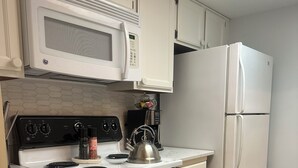 Una cucina con mobili bianchi, un forno a microonde, un piano cottura e un frigorifero.