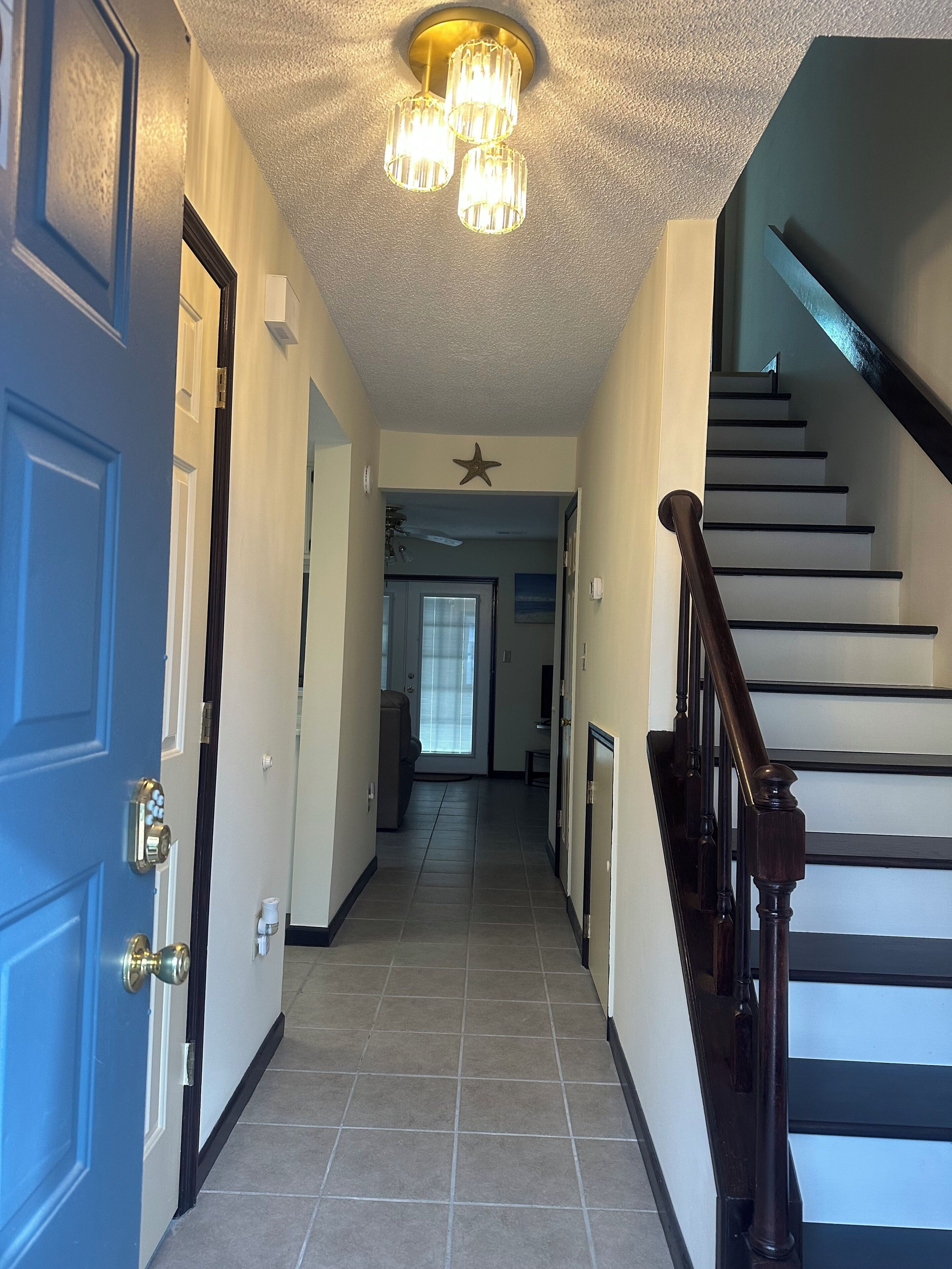 A hallway with a blue door, a staircase with dark railings, and a ceiling light fixture.