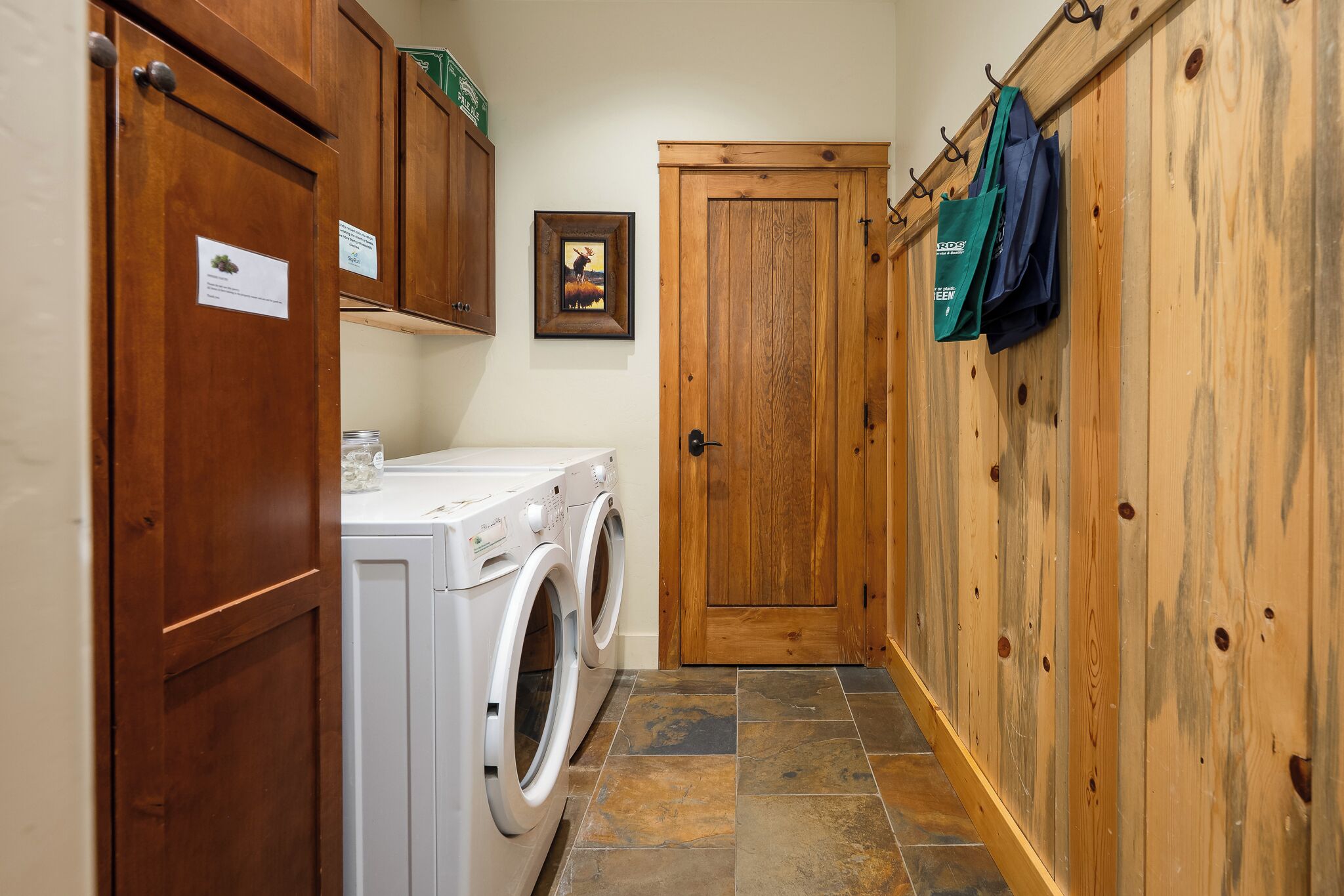 A laundry area with a washing machine, wooden cabinets, a door, and a wall-mounted bag rack.