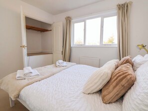 Ein Schlafzimmer mit einem Bett, einem Vorhangfenster, einem Heizkörper und einem geöffneten Kleiderschrank.
