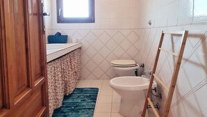 Et badeværelse med toilet, bidet, skab i træ og et vindue.