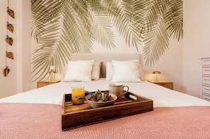 A neatly made bed with a tray of breakfast items, a wall with palm leaf patterns, and a bedside table with a lamp.