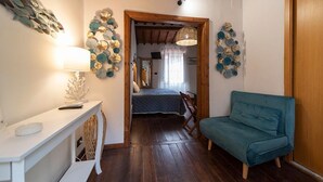 Ein schmales Entree mit einem Bett, einem blauen Sofa, einem weißen Beistelltisch und Wanddekoration.