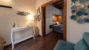 Ein gemütliches Zimmer mit Holzbalkendecke, einem weißen Konsolentisch, einem Bett mit blauer Bettwäsche und einer Wand, die mit runden, metallischen und gläsernen Verzierungen geschmückt ist.