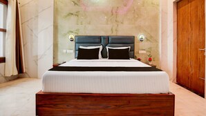 A hotel room with a large bed, marble walls, wooden flooring, and a wooden door.