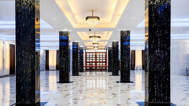 A spacious lobby with marble flooring, tall columns, and a central chandelier.