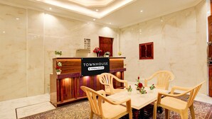 A reception area with a marble wall, a wooden reception desk, and a table with plastic chairs.