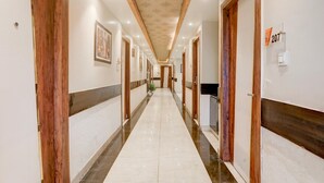A hotel hallway with wooden doors, a tiled floor, and a patterned ceiling.