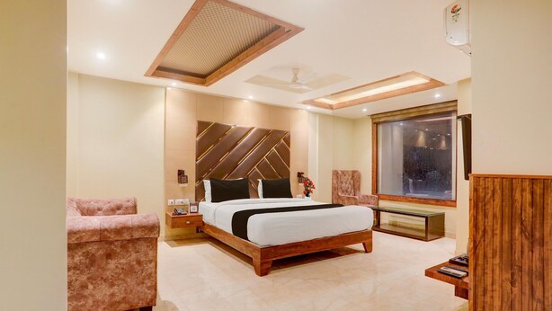 A modern bedroom with a large bed, a chaise lounge, a wooden desk, and a large window.