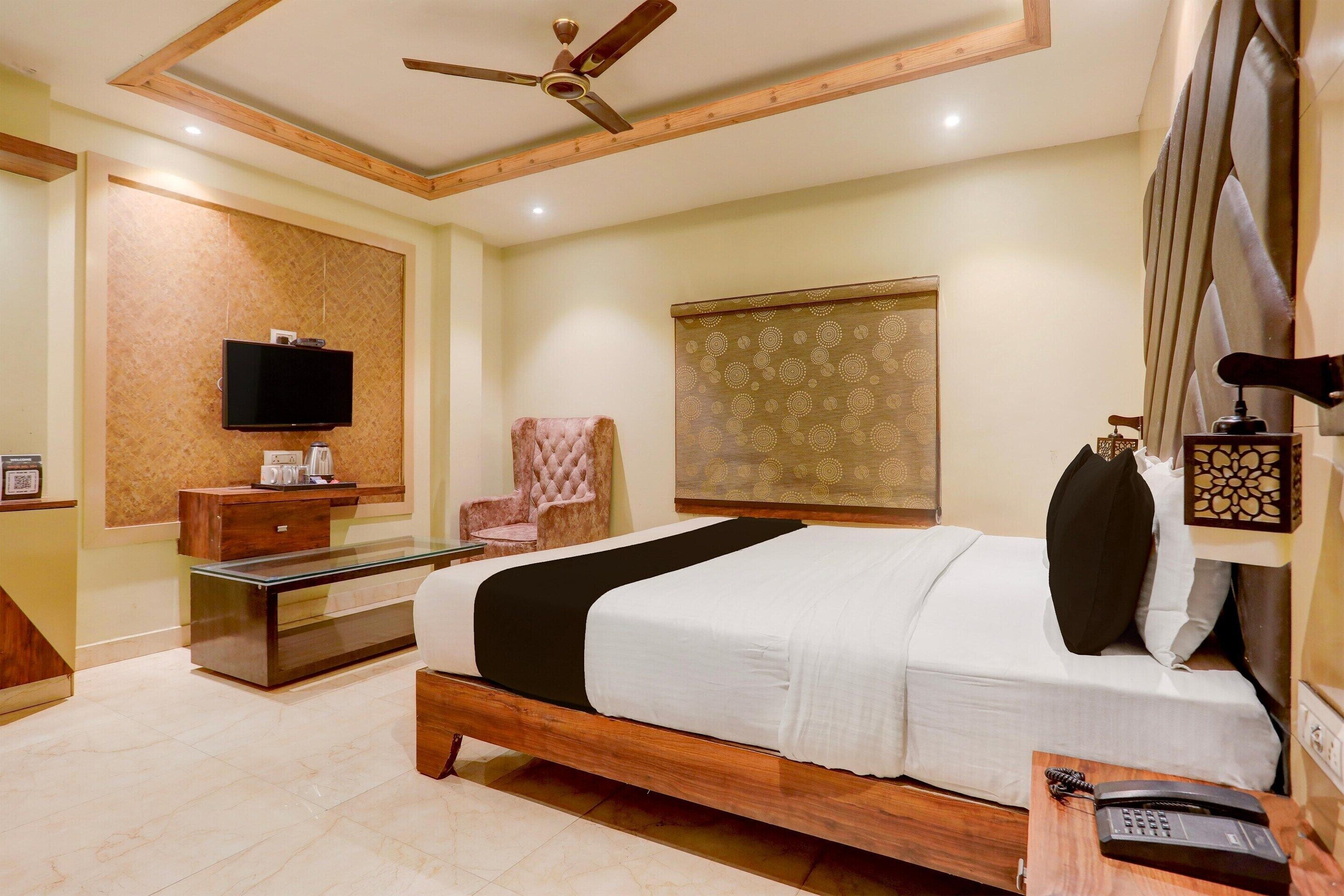 A hotel room with a bed, a TV, a desk with a phone, a chair, and a ceiling fan.