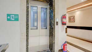 An elevator with a fire exit sign, a fire extinguisher mounted on the wall, and a marble floor.