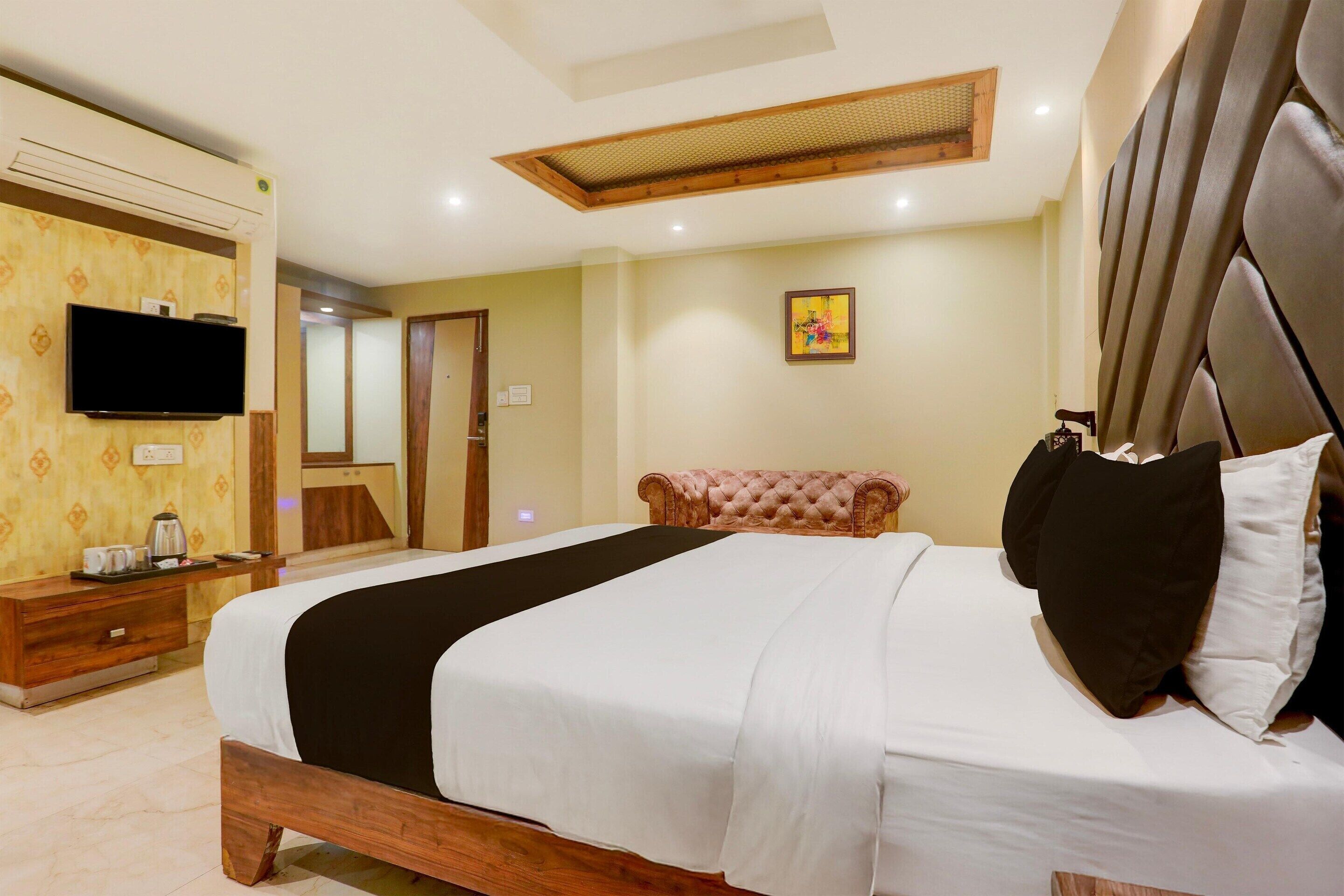 A hotel room with a bed, a television, a desk with a coffee maker, and a mirror.
