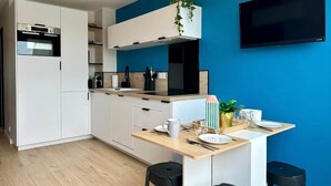 Una cocina moderna con armarios blancos, horno integrado, microondas y televisor negro montado en la pared.
