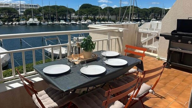 Terraza con una mesa lista para cuatro personas, con vista a un puerto deportivo lleno de barcos.