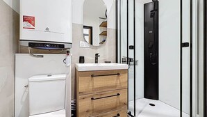Un baño moderno con inodoro, tocador con cajones, espejo y ducha con mampara de vidrio.