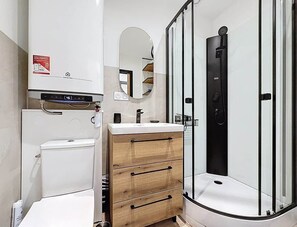 Ein modernes Badezimmer mit Toilette, einem Waschtisch mit Schubladen, einem Spiegel und einer Duschkabine.
