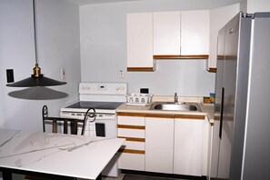 A compact kitchen with white cabinets, a stainless steel refrigerator, a stove, and a sink. - Kingston Horizon Retreat Apt (Kingston)