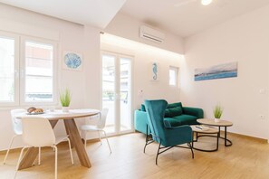 Ein modernes Wohnzimmer mit Essbereich, einem blaugrünen Sofa und Kunstwerken an den Wänden.