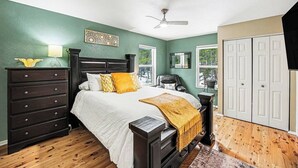 Une chambre à coucher comprenant un lit, une commode, une table de chevet et un ventilateur de plafond.