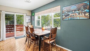 Un coin repas avec une table et des chaises en bois, une grande fenêtre donnant sur un paysage verdoyant et un tableau accroché au mur.