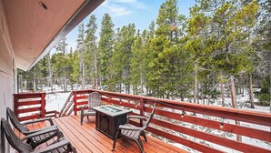 Une terrasse en bois avec des chaises et une table, d’où l’on peut admirer un paysage enneigé parsemé d’arbres.
