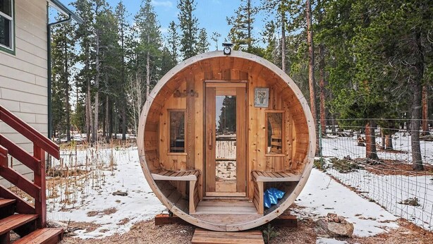Une structure de sauna en bois, dotée de bancs et d’une porte, entourée d’arbres et agrémentée d’une terrasse en bois.