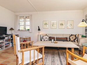 Een woonkamer met een bank, stoelen, een salontafel, een televisie en een boekenkast.
