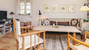 Una sala de estar con sofá, sillas, una mesa de centro, televisor, estantería y ventana.