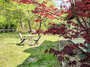 Een gazon met een tafel en stoelen, omringd door bomen met rood herfstblad.