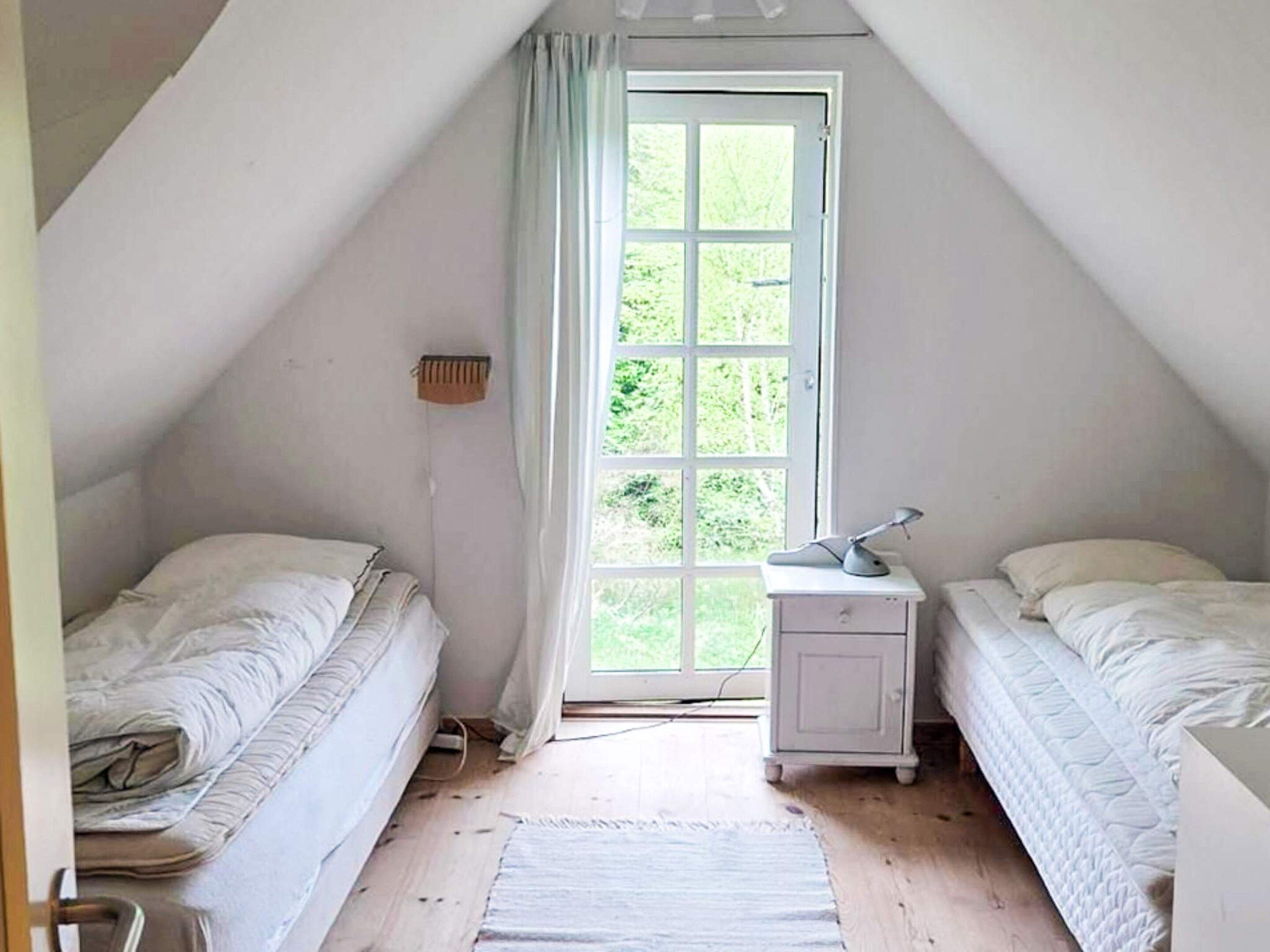 A small, single-room attic bedroom with two beds, a nightstand, and a window.