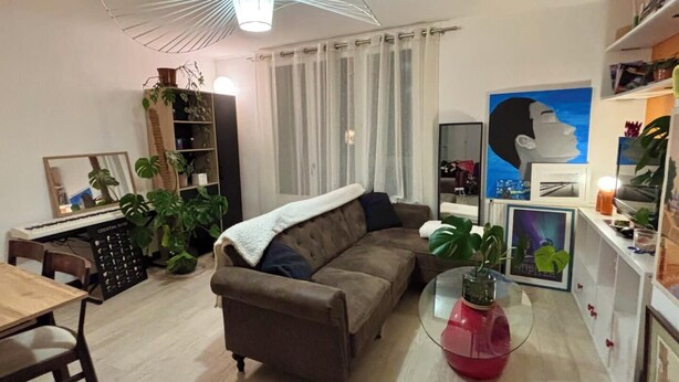Una sala de estar con sofá, mesa de centro, estantería y un amplio ventanal con cortinas.