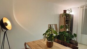 Un comedor con una mesa de madera, sillas, una lámpara de pie y plantas en macetas.