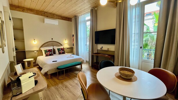 Ein Hotelzimmer mit Bett, Nachttisch, Fernseher, Esstisch, Stühlen und einem fensterbepflanzten Fenster mit Vorhängen.