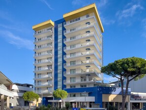 A multi-story building with balconies, a blue and yellow facade, and a clear sky. - Bright Flat in Piazza Fontana (Lignano Sabbiadoro)